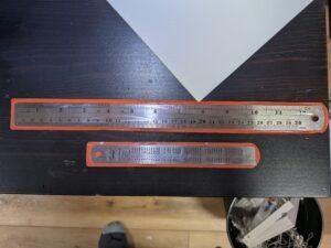 a set of 2 metal rulers of different sizes, each in a small sleeve